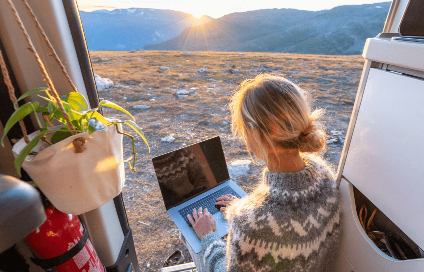 A person working on their computer on a van with a mountain view